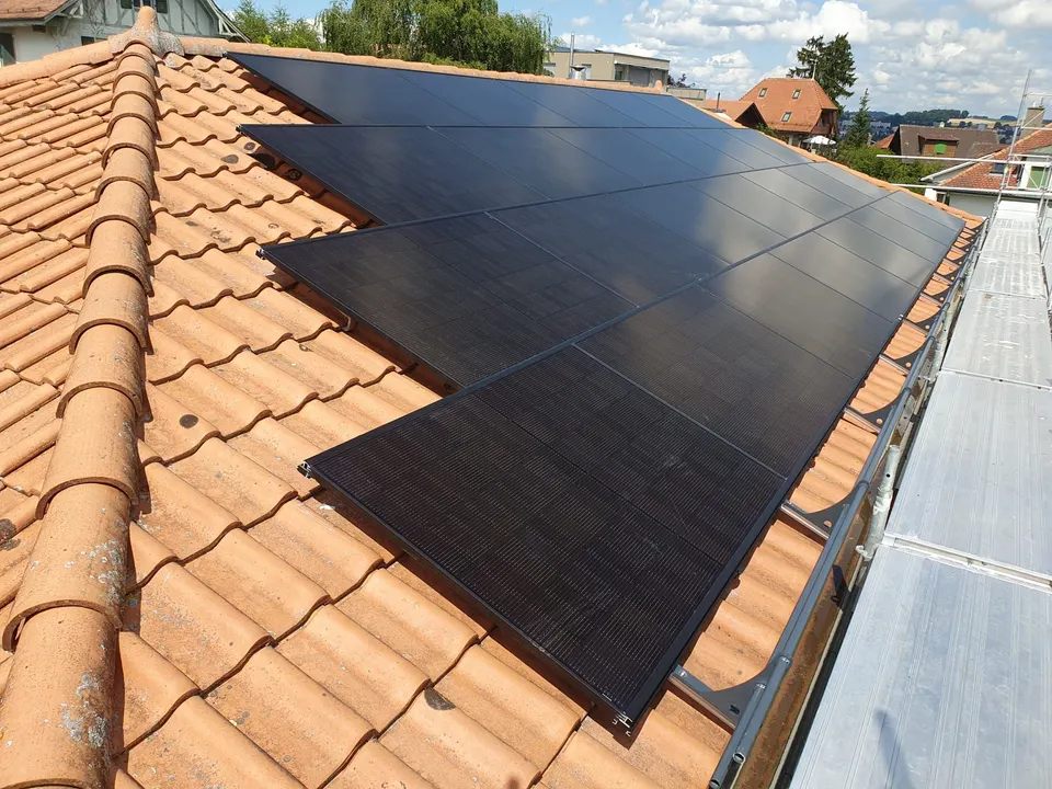 Schwarze Solarmodule auf dem roten Ziegeldach eines Mehrfamilienhauses in Freiburg – Gerüst noch am Gebäude