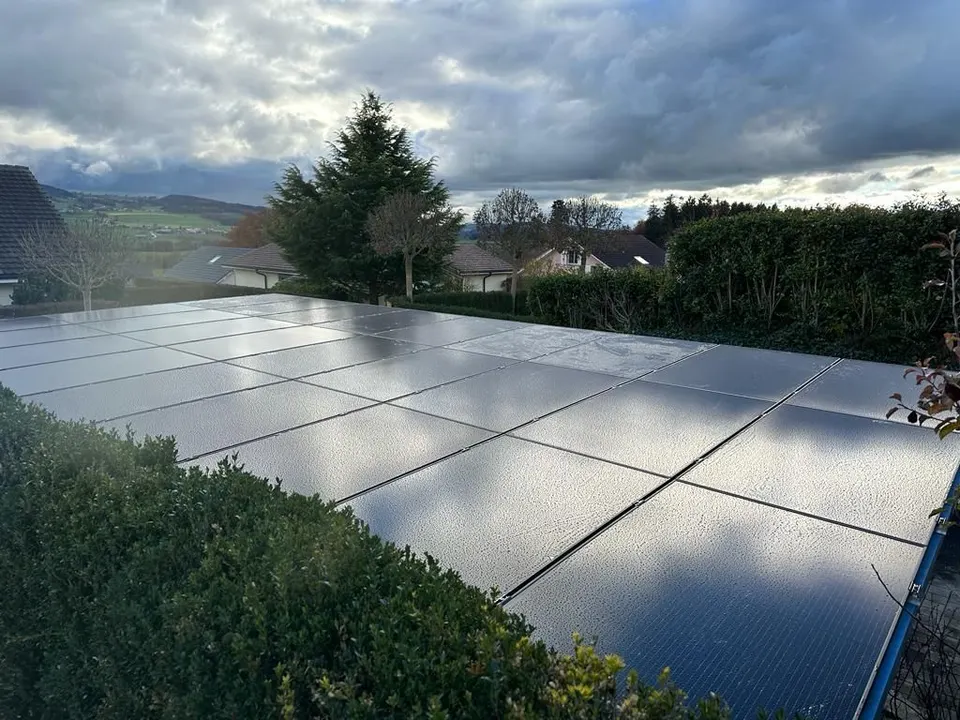 Modules solaires noirs sur le toit en tuiles grises d’une maison individuelle à Chénens (environs : prés, arbres)