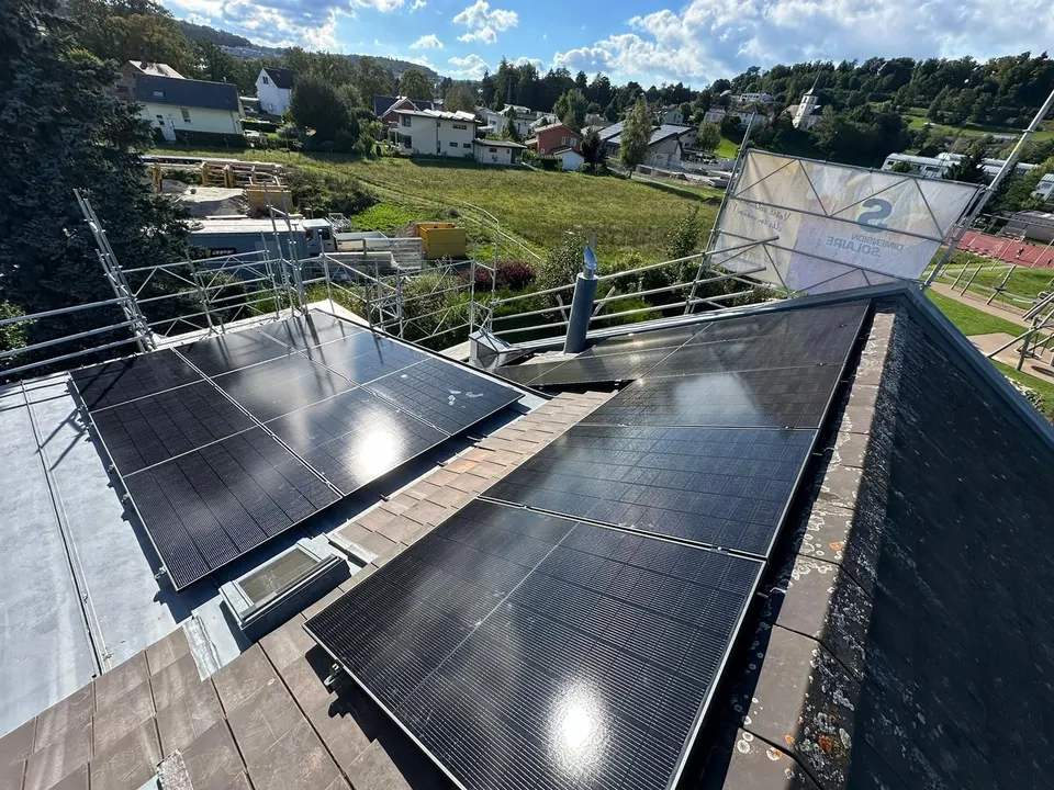 Modules solaires noirs sur le toit en tuiles grises d’une maison individuelle à Matran (environs : maisons voisines, arbres)