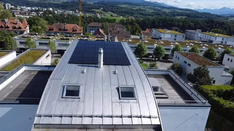 Vue aérienne : modules solaires noirs sur le toit plat d’une maison individuelle à Villars-sur-Glâne (environs : maisons voisines, montagnes)