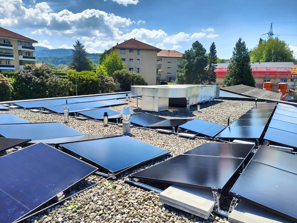 Modules solaires noirs sur le toit plat d’une maison individuelle à Bossonnens (environs : maisons voisines)