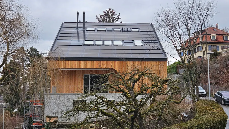 Fertige Anlage: Mehrfamilienhaus in Freiburg mit Holzfassade und dunkler Indach-Solaranlage, Bäume im Vordergrund