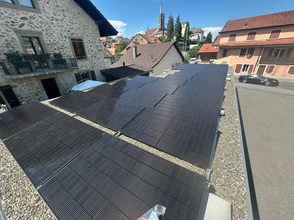 Modules noirs sur le toit plat gravillonné de l’immeuble à Châtel-St-Denis, maisons du village et clocher en arrière-plan