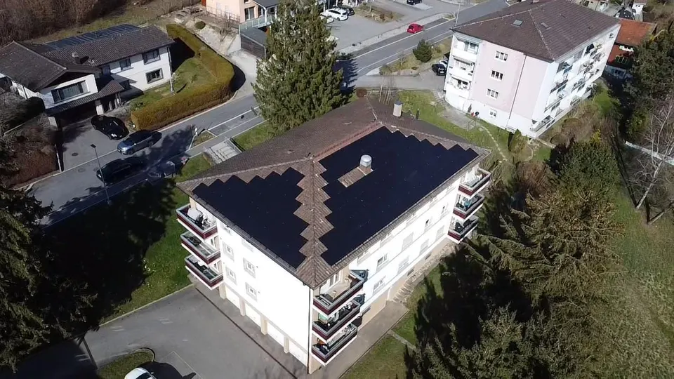 Vue aérienne : modules solaires noirs sur le toit en tuiles sombres d’une maison individuelle à Matran (environs : maisons voisines) – autre vue