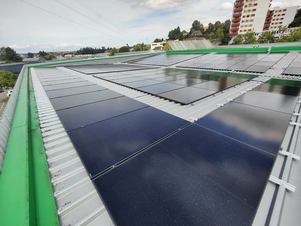 Rangées de modules noirs sur le toit en tôle du bâtiment commercial à Givisiez, rive verte, immeubles en arrière-plan