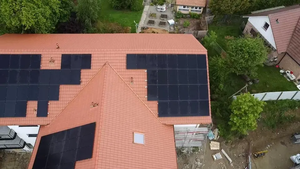 Vue aérienne : champs de modules noirs sur le toit en tuiles rouges de l’immeuble à Cottens, jardin et maisons voisines