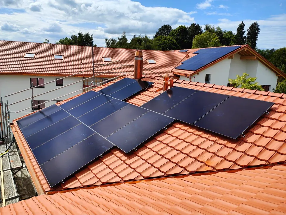 Modules solaires noirs sur le toit en tuiles rouges d’un immeuble à Cottens (environs : maisons voisines)