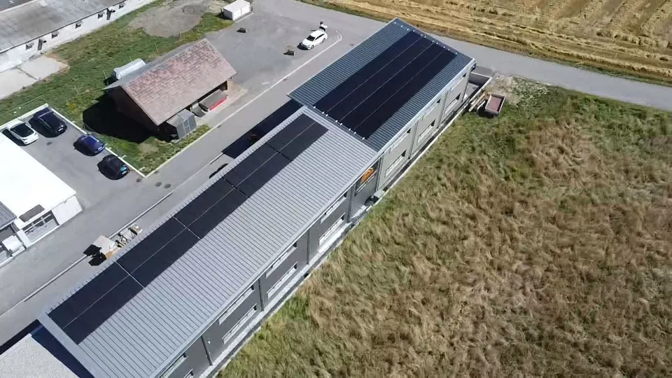 Vue aérienne : modules solaires noirs sur le toit en tôle d’une halle à Cournillens (environs : prés) – autre vue