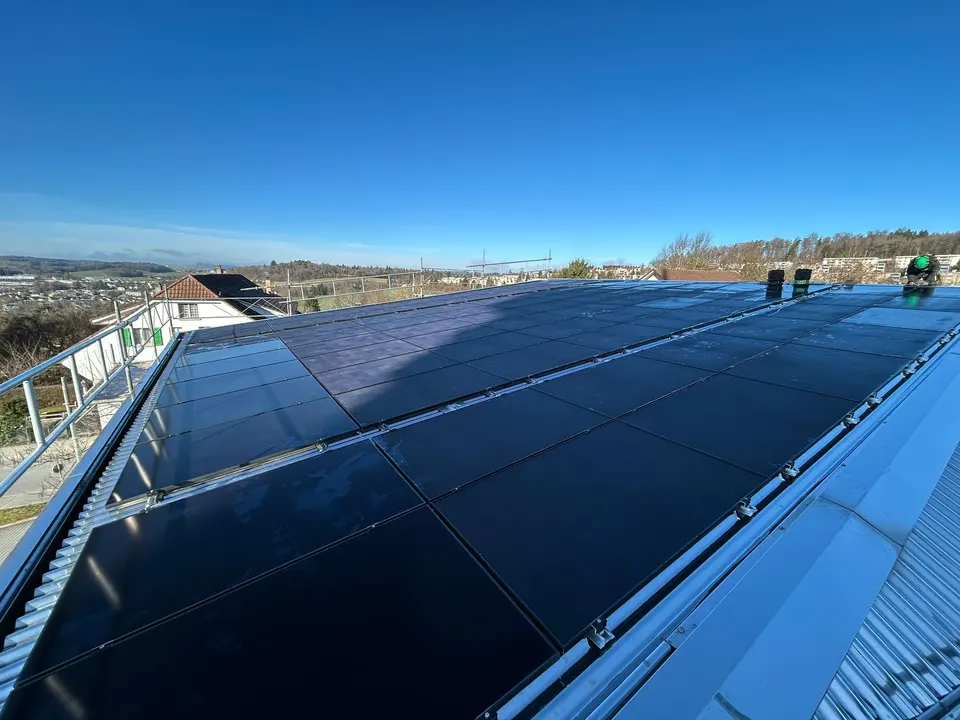 Installation terminée : modules solaires noirs sur le toit en tôle d’un bâtiment public à Villars-sur-Glâne, vue sur la campagne, ciel bleu