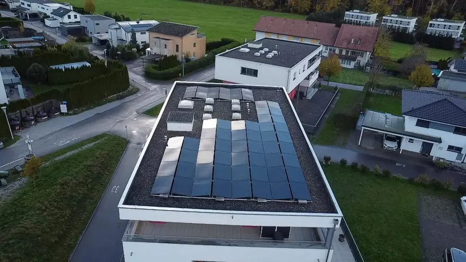 Vue aérienne : modules solaires noirs sur le toit plat d’un immeuble en PPE à Bulle (environs : maisons voisines)