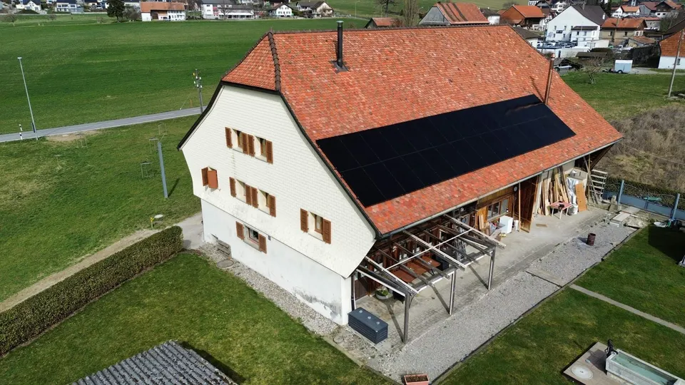 Vue aérienne : modules solaires noirs sur le toit en tuiles rouges d’une ancienne ferme à Chénens (environs : prés)