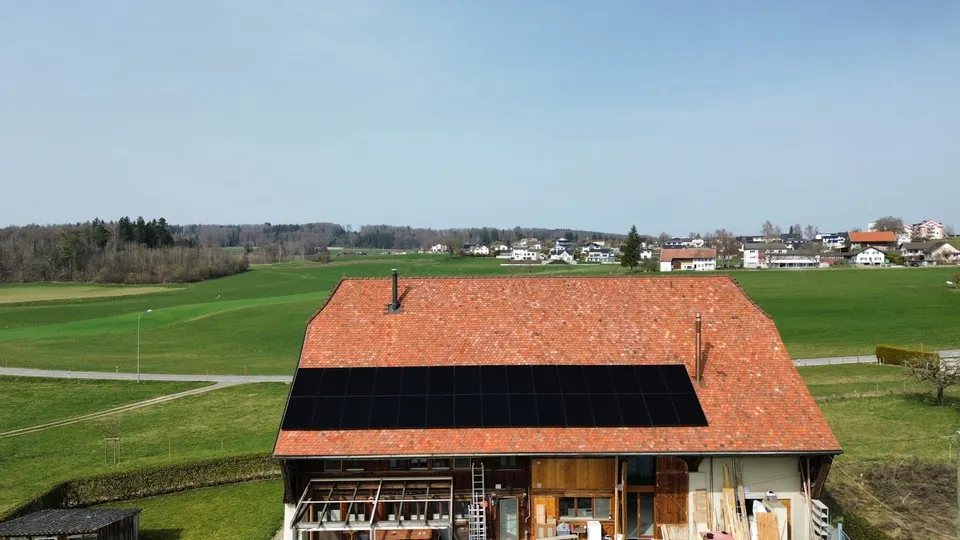 Vue aérienne : modules solaires noirs sur le toit en tuiles rouges d’une ancienne ferme à Chénens (environs : prés) – autre vue