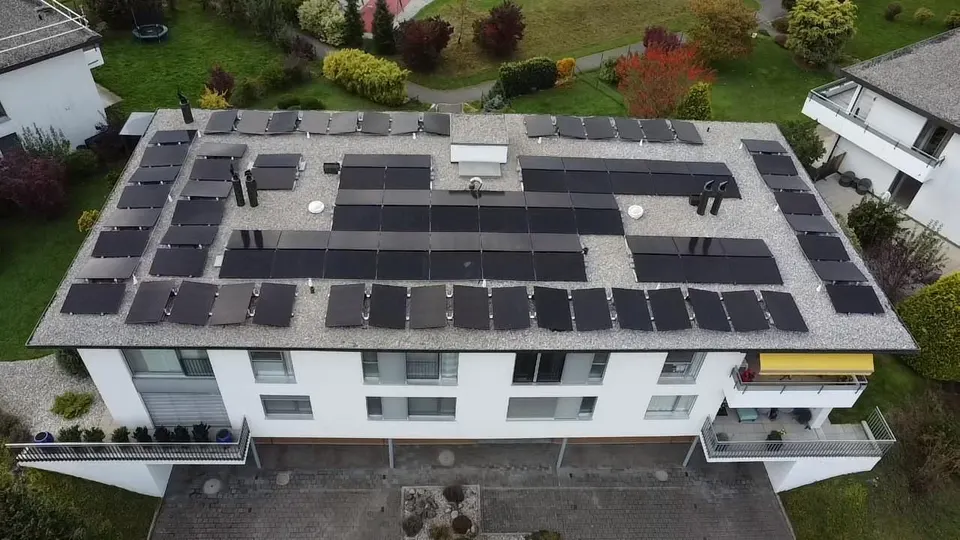 Vue aérienne : immeuble à Bulle avec rangées de modules noirs sur le toit plat, jardin autour