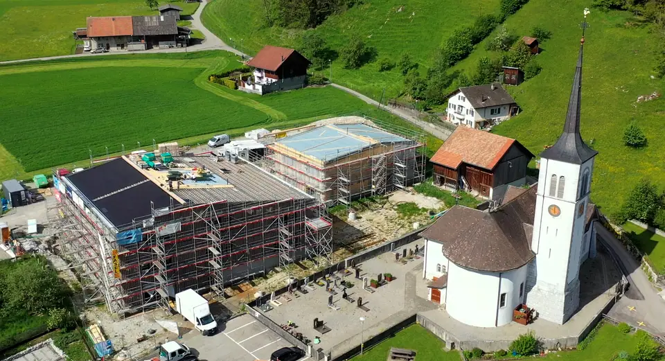 Luftbild: Schulhaus Neirivue mit schwarzer Indach-Solaranlage neben der Dorfkirche