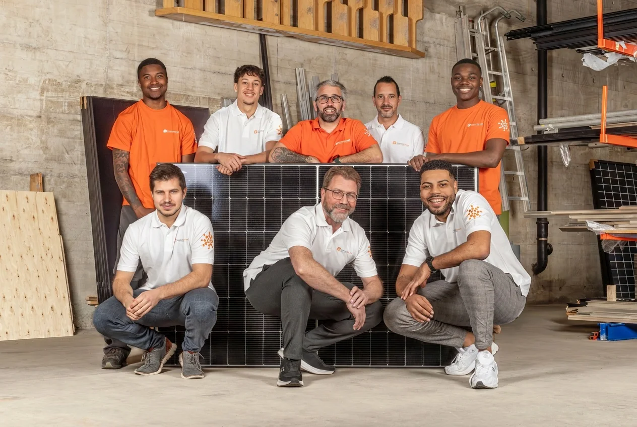 Das Team von Dimension Solaire – Monteure in Orange und Büroteam in Weiss – um ein Solarmodul gruppiert